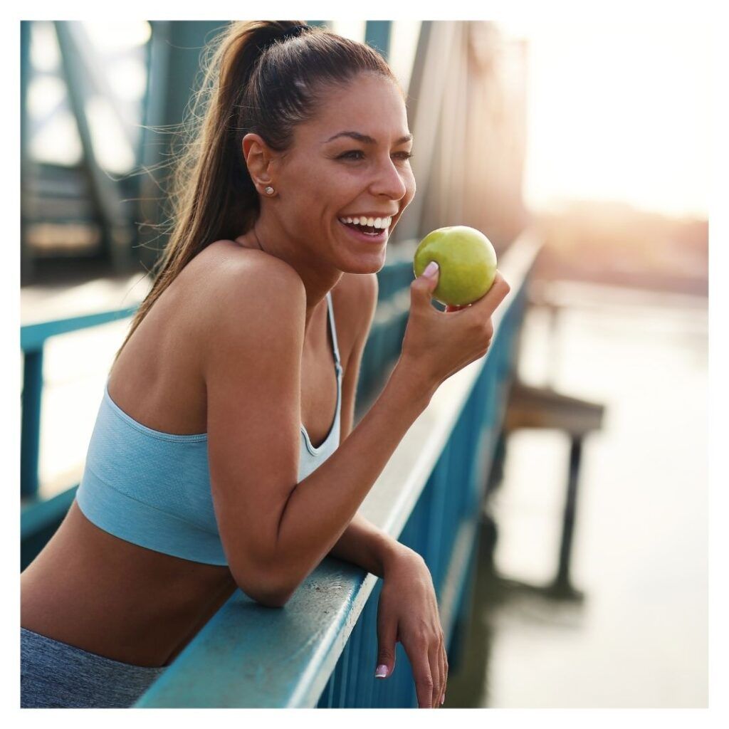 a woman smiling on a bridge eating an apple